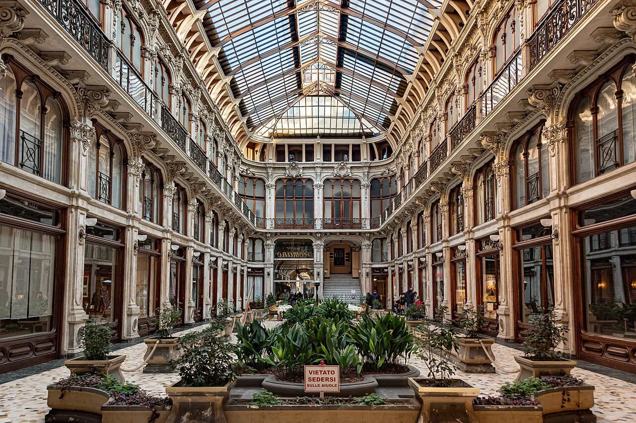 The glass-roofed 19th-century Galleria Subalpina arcade in Turin, with ornate balconies and potted plants