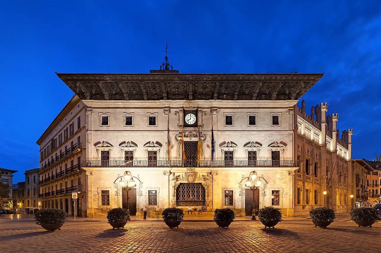 Palma de Mallorca City Hall lit up at dusk on the cobbled Plaça de Cort in the old town