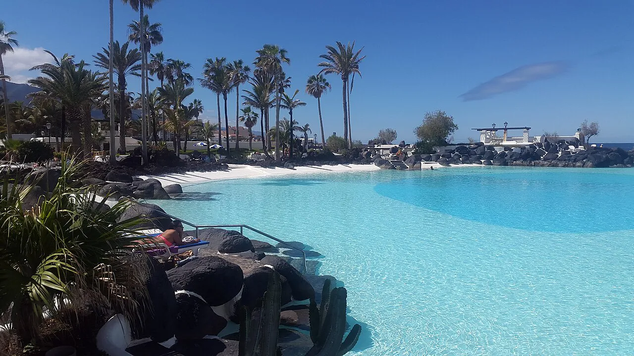 Turquoise saltwater pools edged by black volcanic rock and palms at Lago Martiánez, Puerto de la Cruz