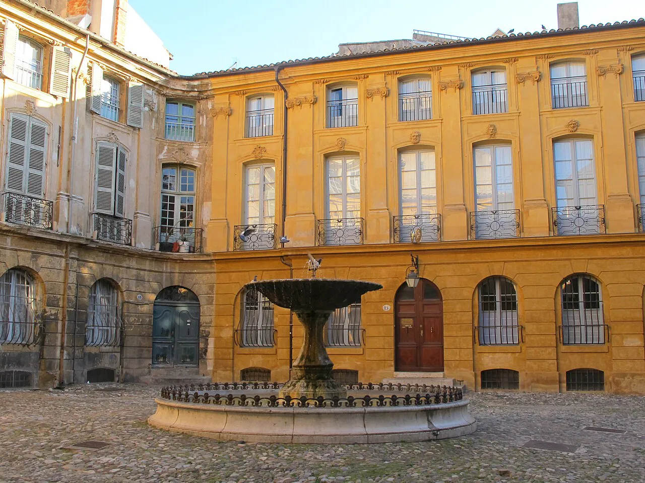 Fountain in the cobbled Place d’Albertas framed by honey-coloured mansion facades, Aix-en-Provence