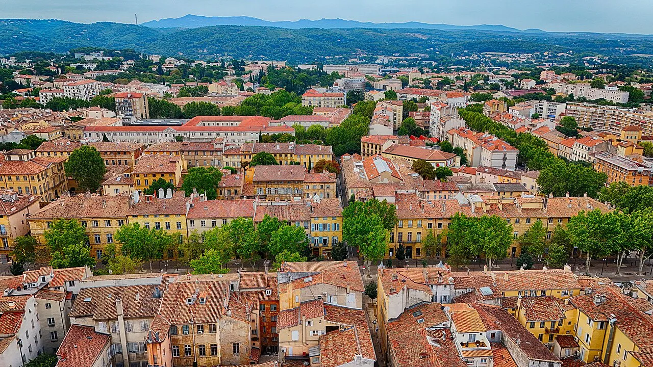 Aerial view over the terracotta rooftops and plane trees of Aix-en-Provence toward distant hills