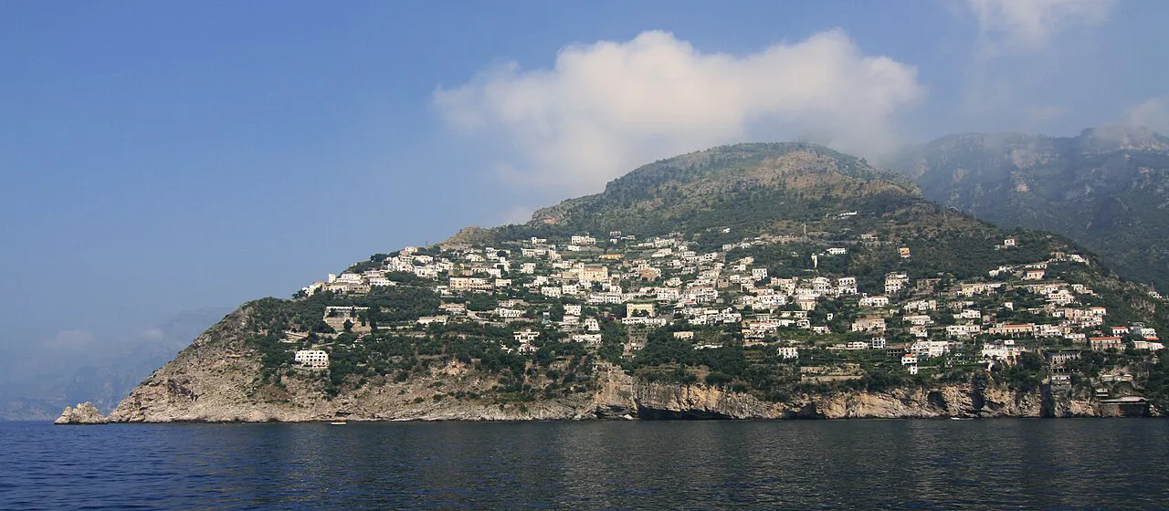 Praiano's white houses spread over a green headland above the sea, seen from the water