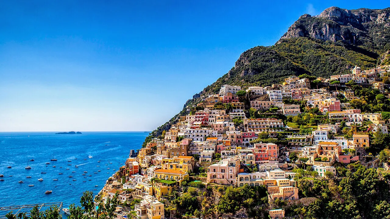 Colourful houses of Positano climbing a steep green hillside above a sea dotted with boats