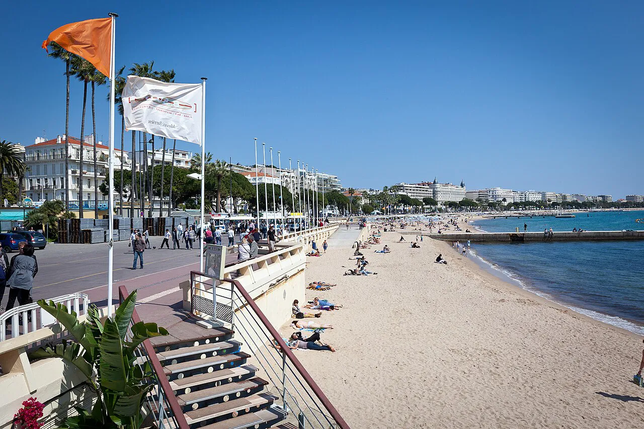 Sandy beach below the Croisette promenade in Cannes, with steps down from the palm-lined walkway
