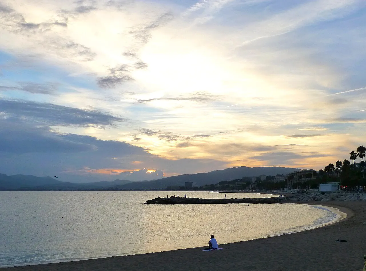 Plage du Midi in Cannes at sunset, a long public sandy shore curving toward the Esterel