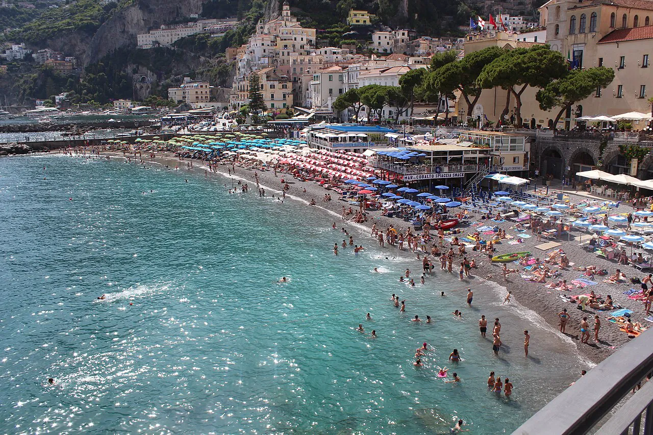 Turquoise water and the busy pebble beach of Amalfi below the town's hillside buildings