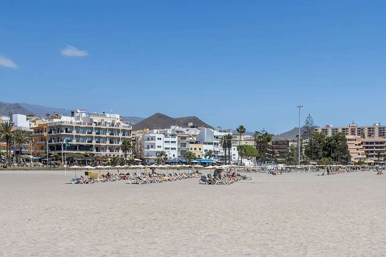Wide sandy beach at Playa Honda in Los Cristianos with seafront buildings and mountains behind, Tenerife