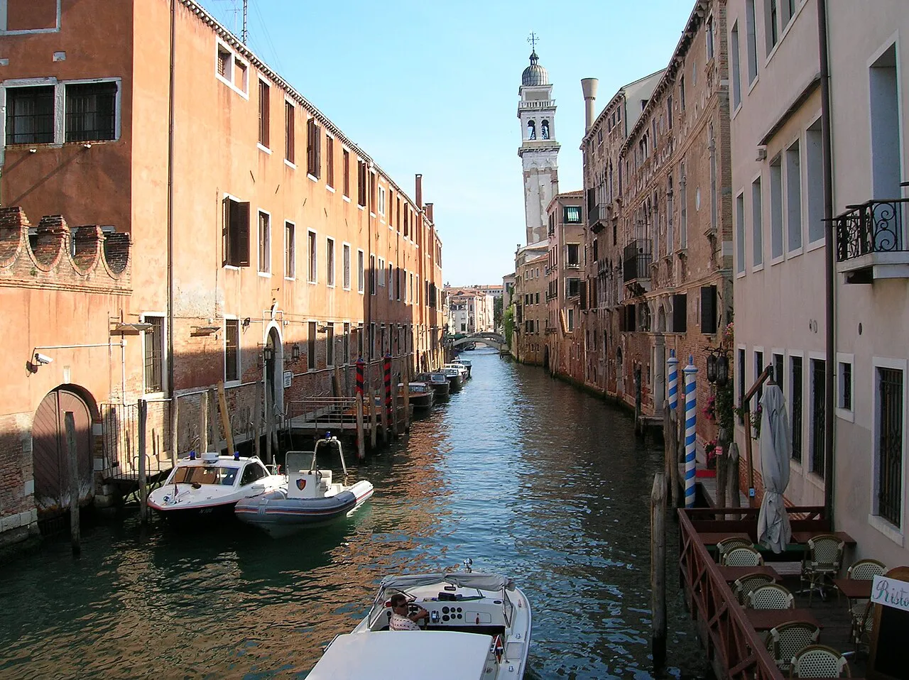 Quiet canal in Castello, Venice, with moored boats and the leaning bell tower of San Giorgio dei Greci