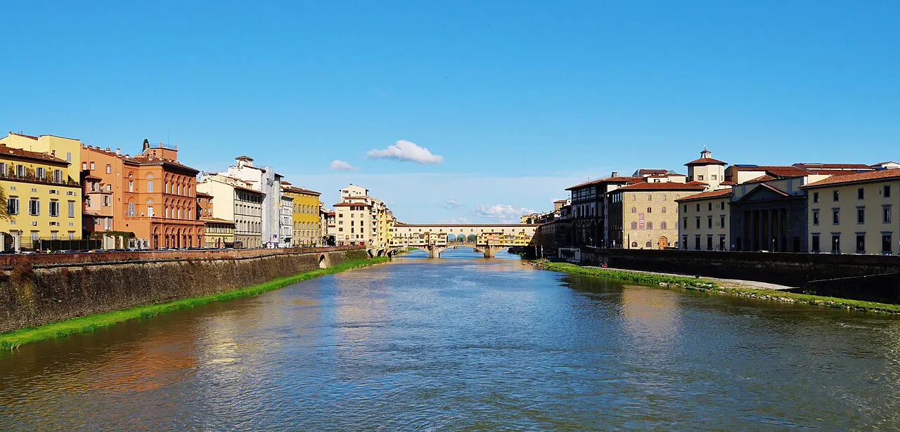 The Arno in Florence between colourful riverside buildings, with Ponte Vecchio in the distance