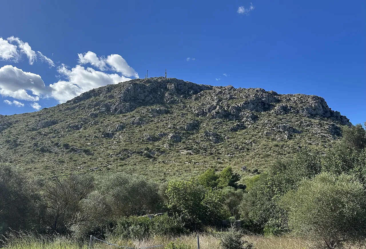 The rocky, scrub-covered Puig de Sant Martí hill near Alcúdia under a blue sky with white clouds