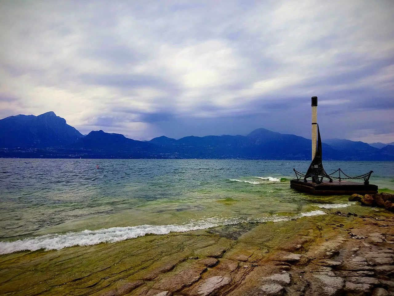 Smooth limestone shore and clear water at Torri del Benaco, with mountains across Lake Garda