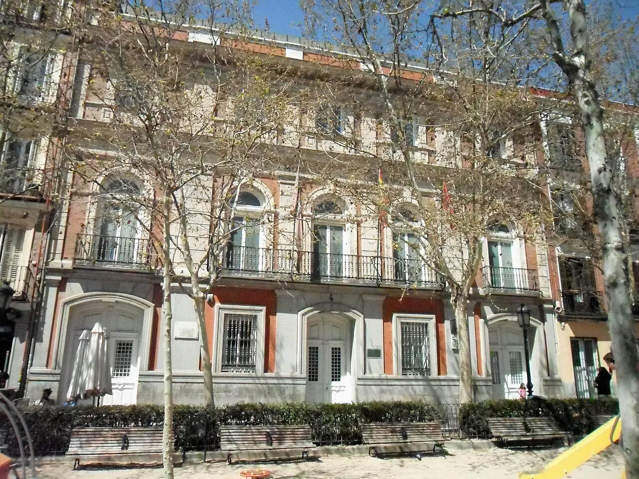 Brick and stone façade of the Chamberí district hall behind bare trees on Plaza de Chamberí, Madrid