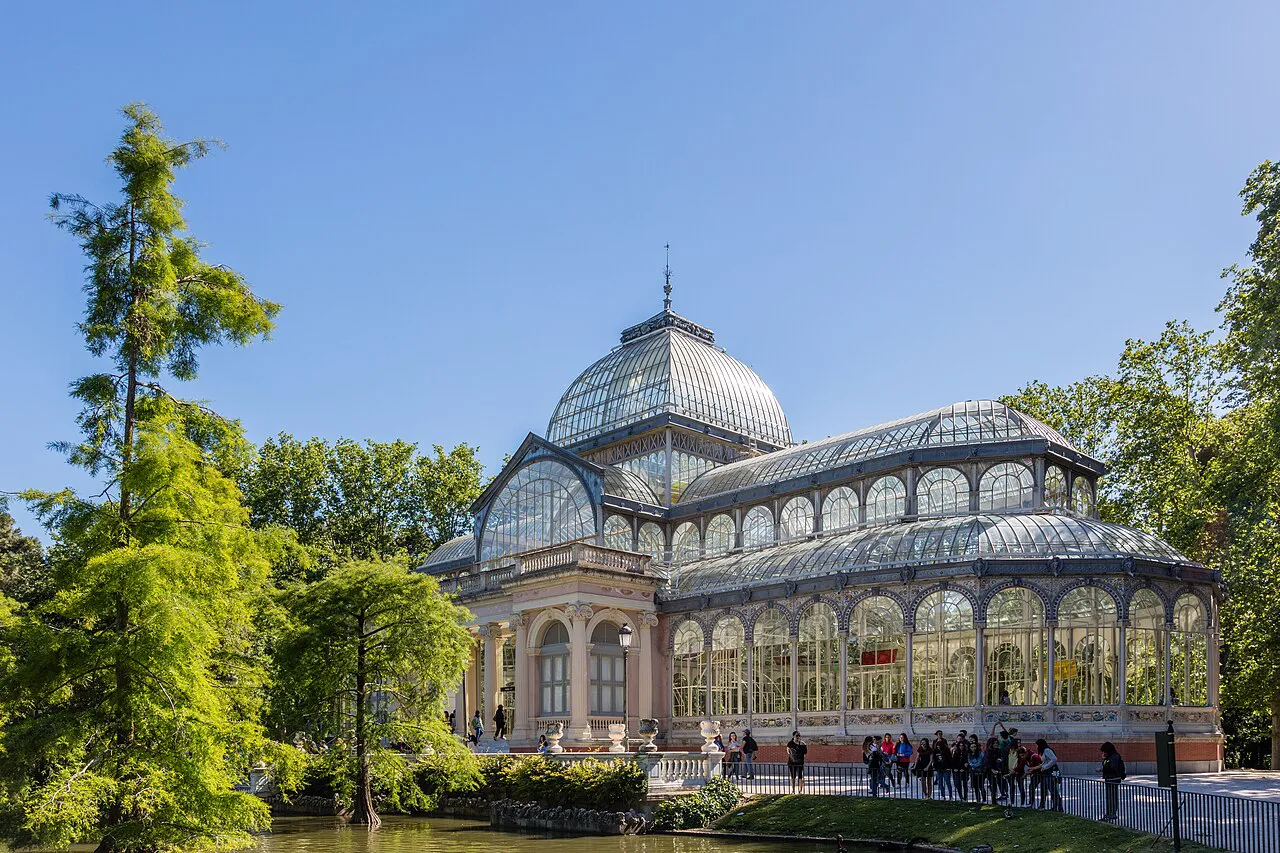 Glass and iron Palacio de Cristal among green trees in Madrid’s Retiro Park under a blue sky