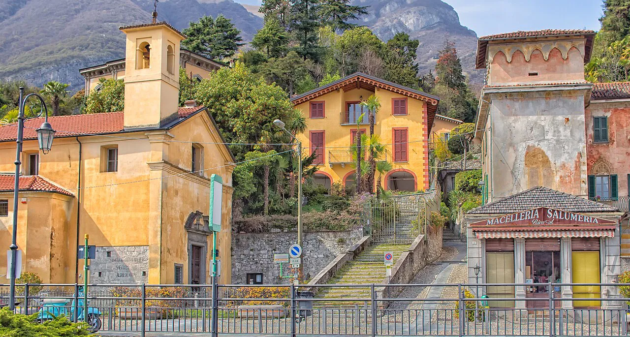 Yellow church of St Bartholomew and a stepped lane between old buildings in Tremezzo, Lake Como