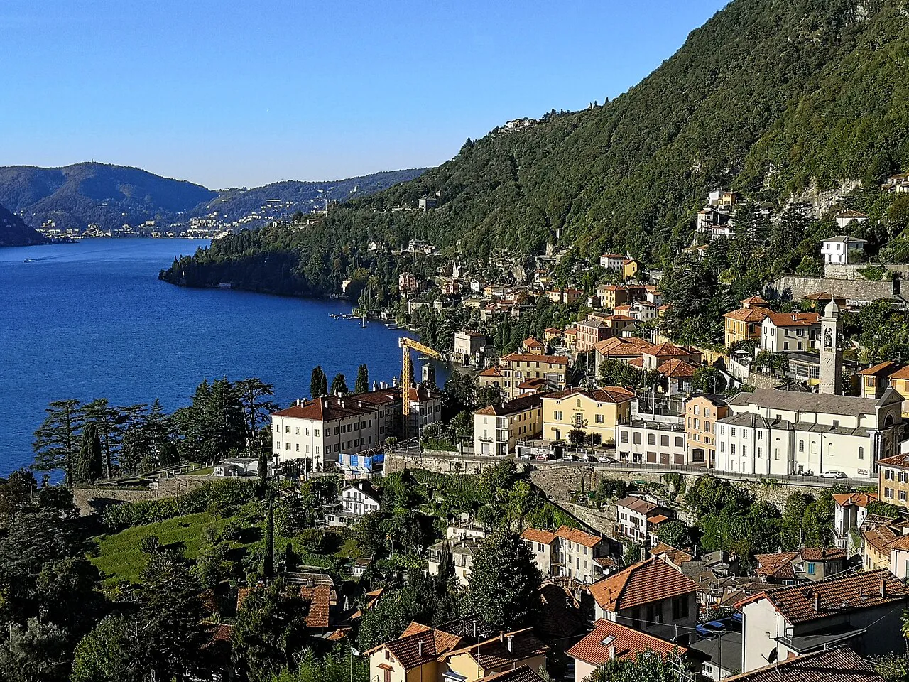 Moltrasio’s church and houses on the steep wooded shore of Lake Como in morning light