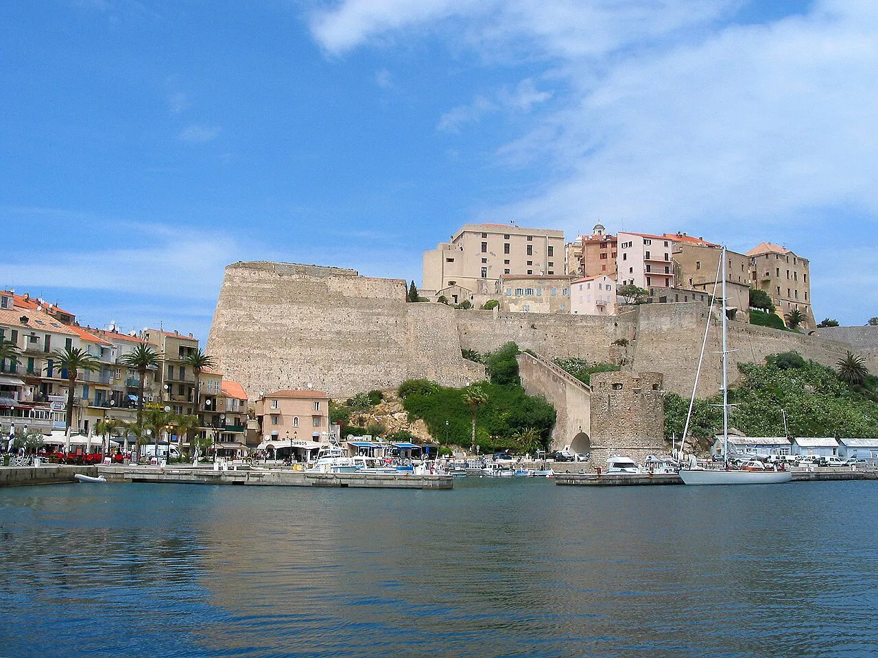 Calvi citadel walls rising above the harbour and waterfront buildings under a blue sky