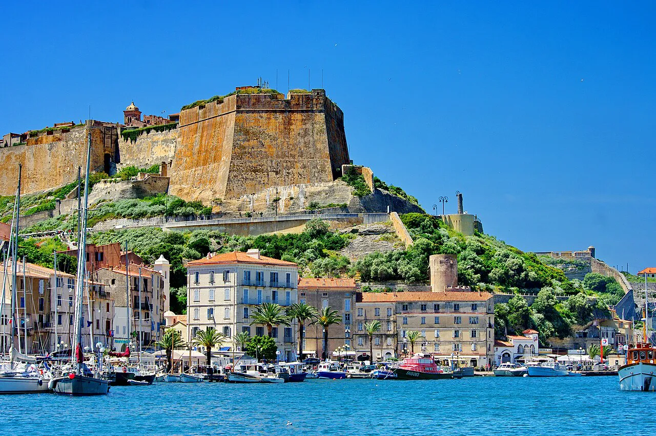 Bonifacio marina with boats and pastel quayside buildings below the hilltop citadel bastion