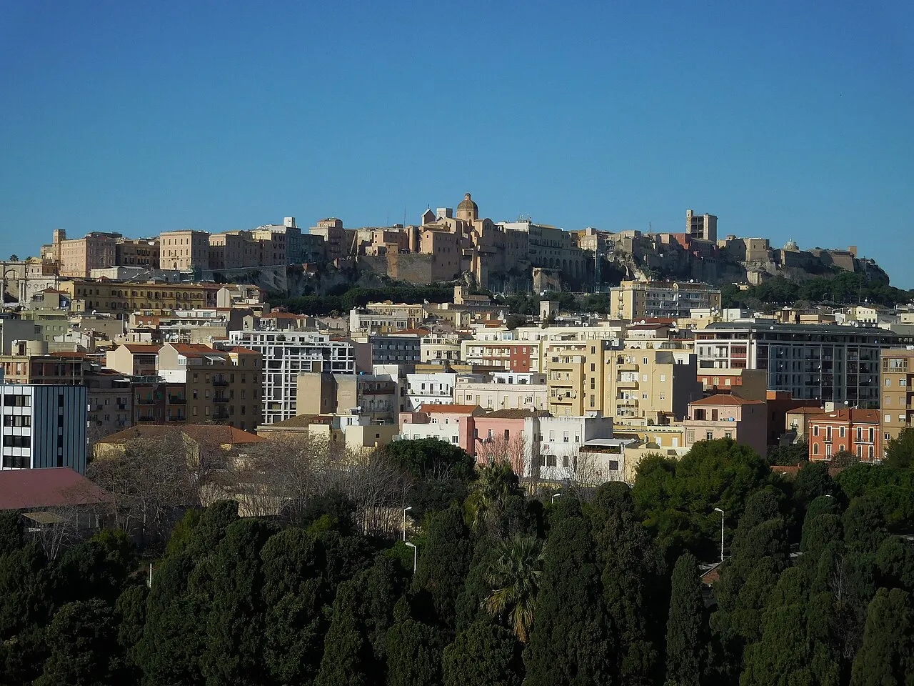 The walled Castello quarter of Cagliari rising above the modern city under a clear blue sky, Sardinia