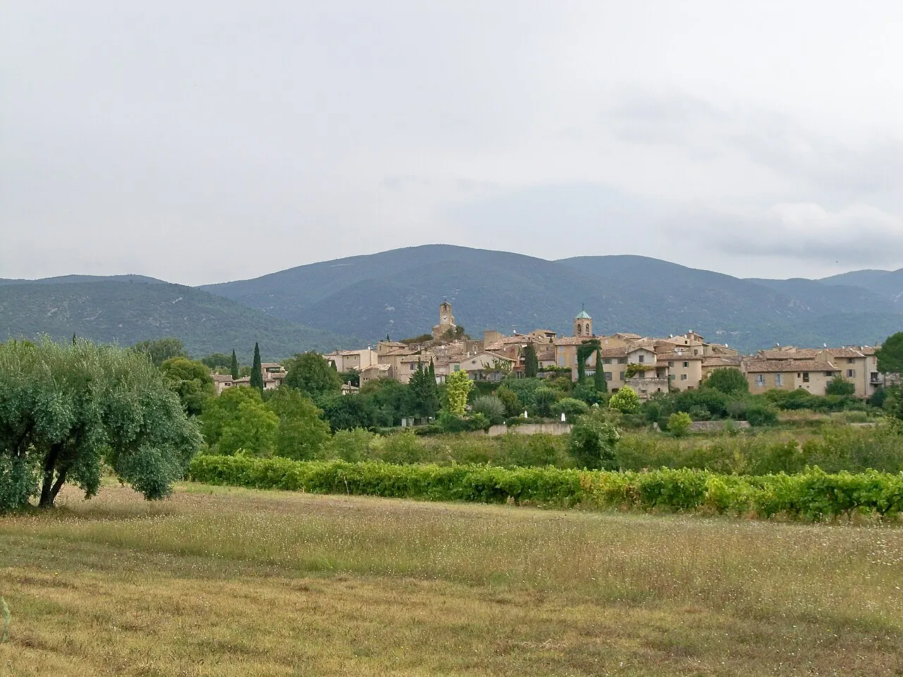Lourmarin village beyond fields and olive trees, with the Luberon hills behind