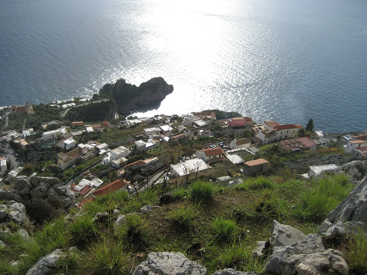 Rooftops of Conca dei Marini seen from the rocky slopes above, with the sunlit sea beyond