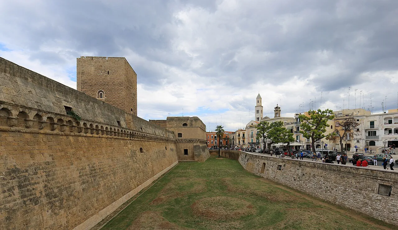 Massive stone walls and grassy moat of the Castello Svevo, with Bari old town buildings beyond