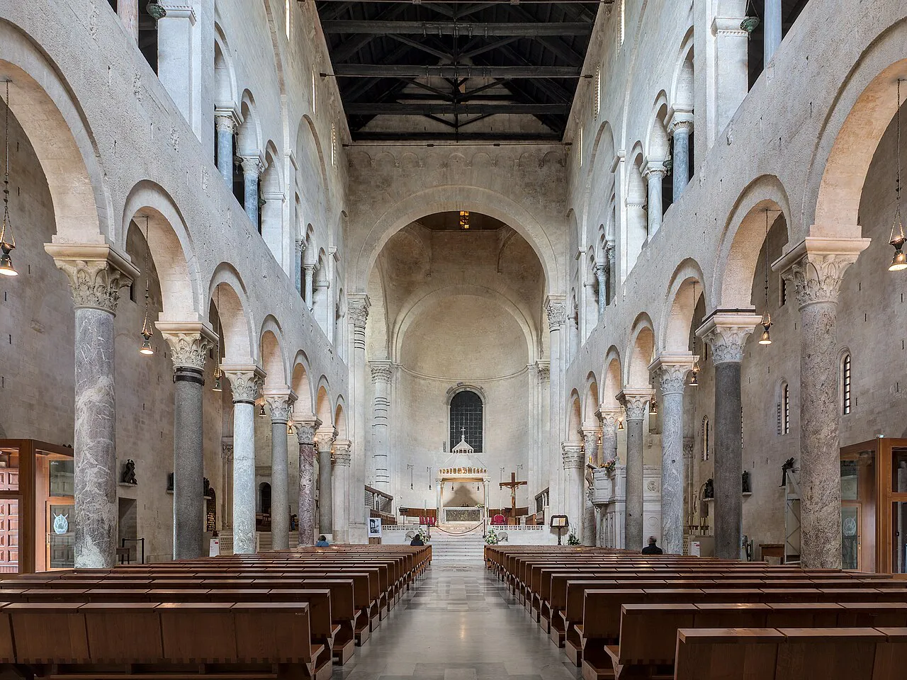 The pale stone Romanesque nave of the Cathedral of San Sabino in Bari, lined with arches and columns