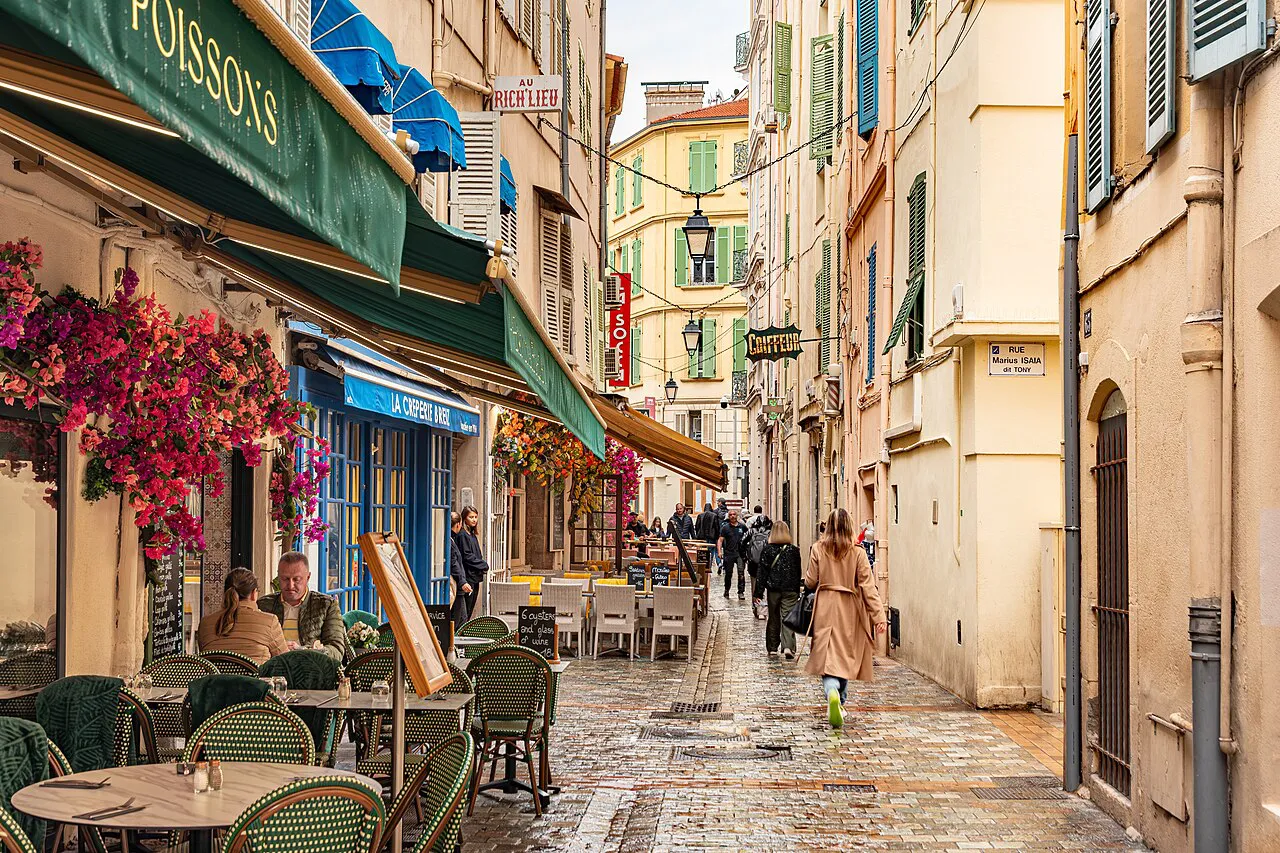 Narrow paved lane in central Cannes lined with pastel facades, bougainvillea and café terraces