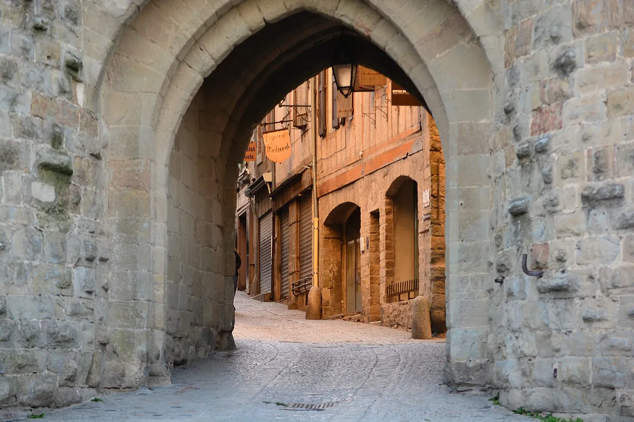 Pointed stone archway of the Porte Narbonnaise framing a sunlit street inside the Cité de Carcassonne