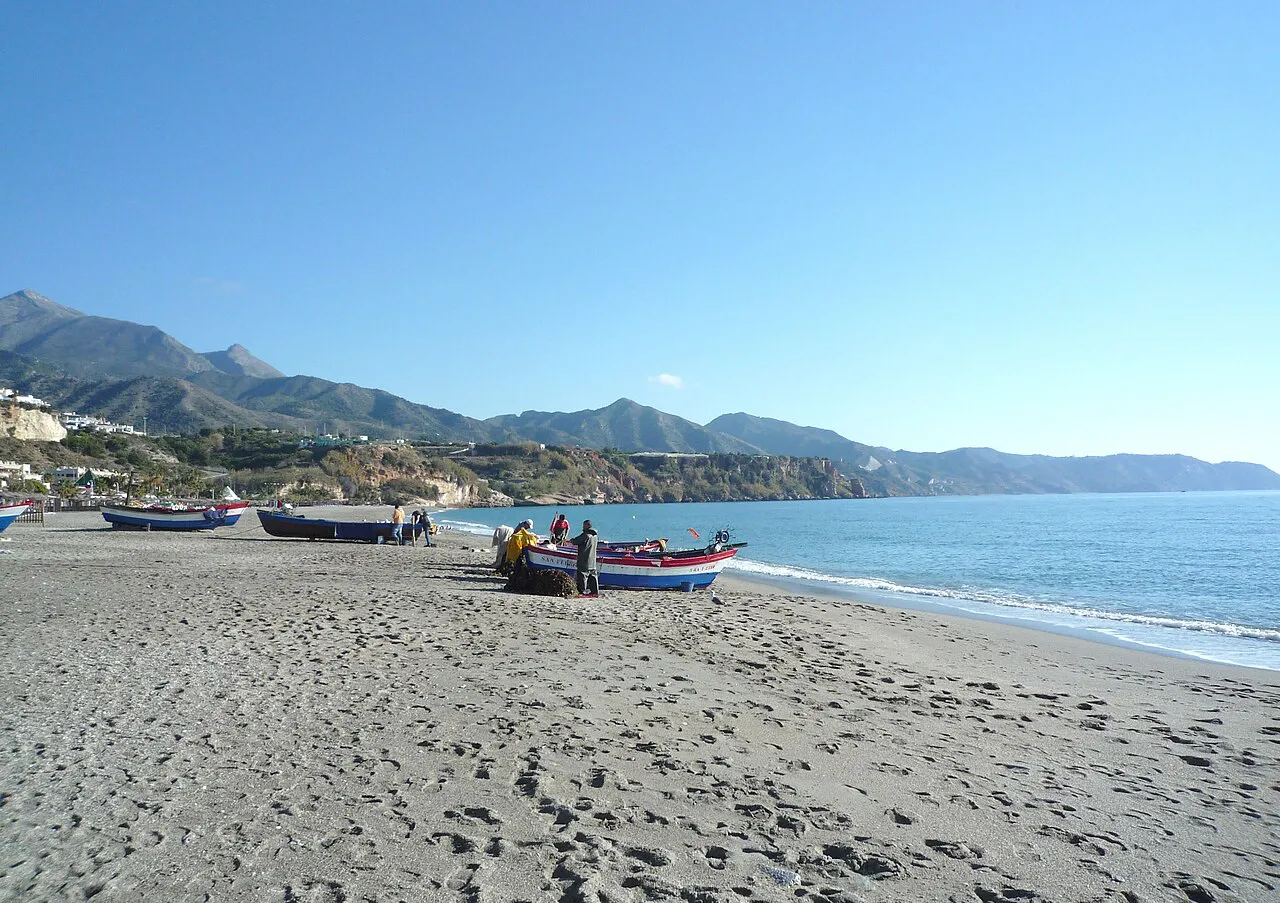 Fishing boats pulled up on the sand at Burriana beach in Nerja, with mountains along the coast