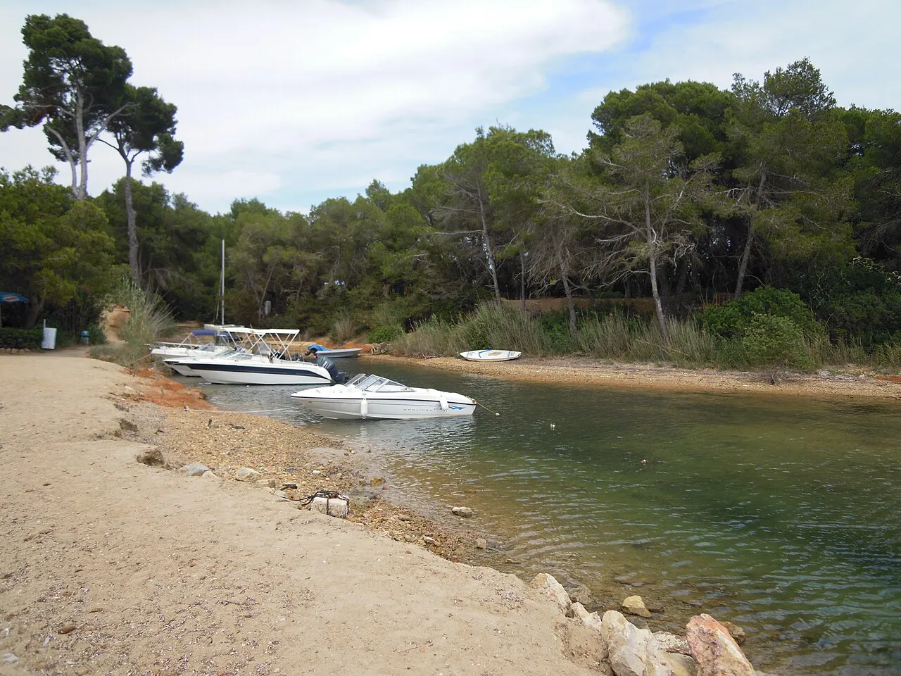 Shallow creek with moored motorboats beside the pine-backed sand at Es Niu Blau, near Santa Eulària des Riu