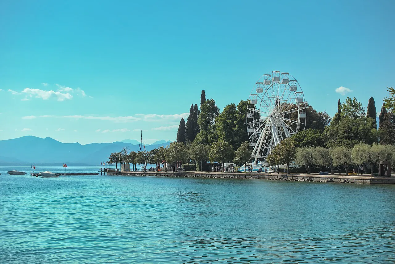 Turquoise Lake Garda water and a tree-lined point with a Ferris wheel at Bardolino