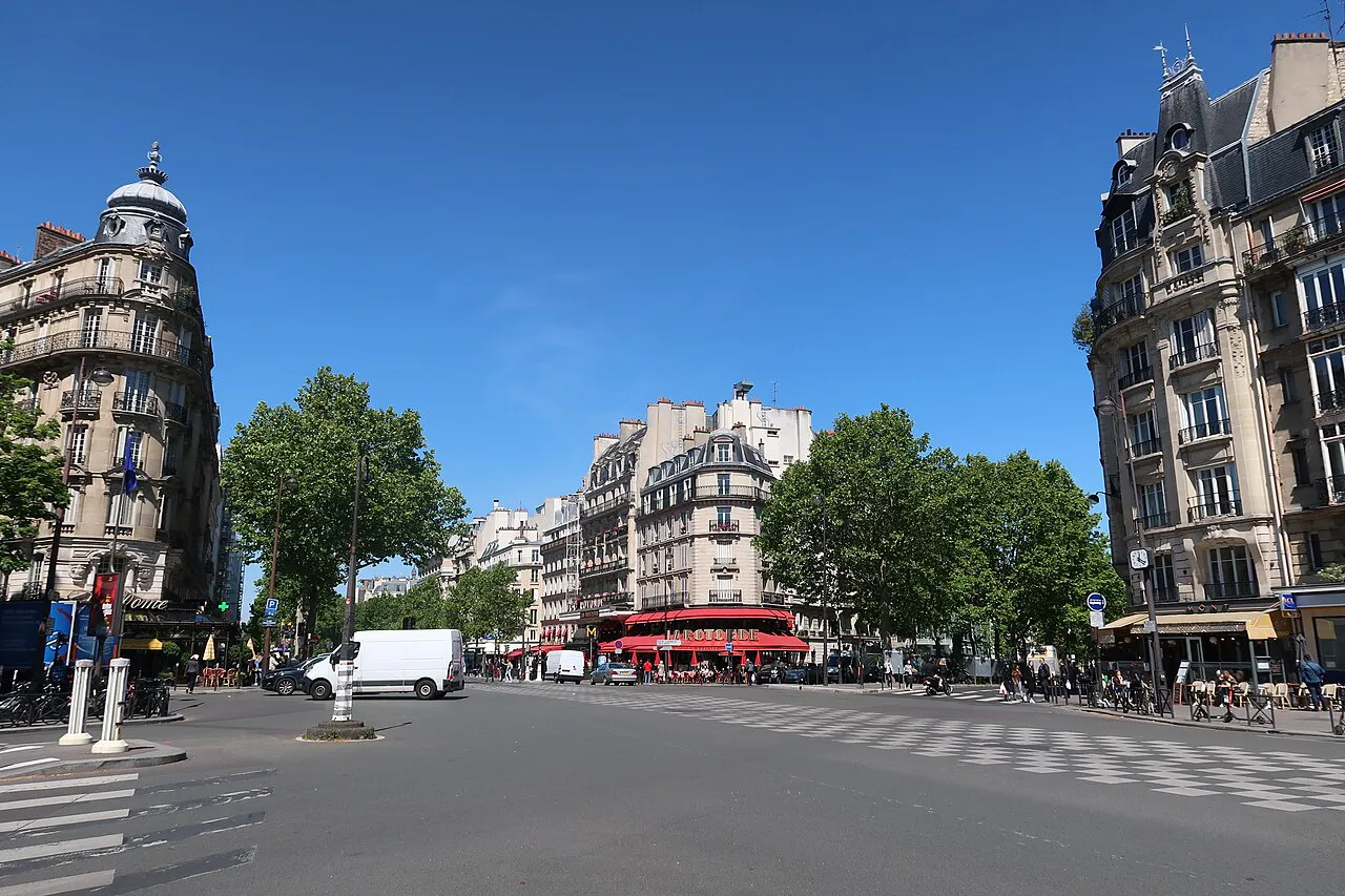 Carrefour Vavin crossroads with corner Haussmann buildings under a blue sky, Montparnasse, Paris