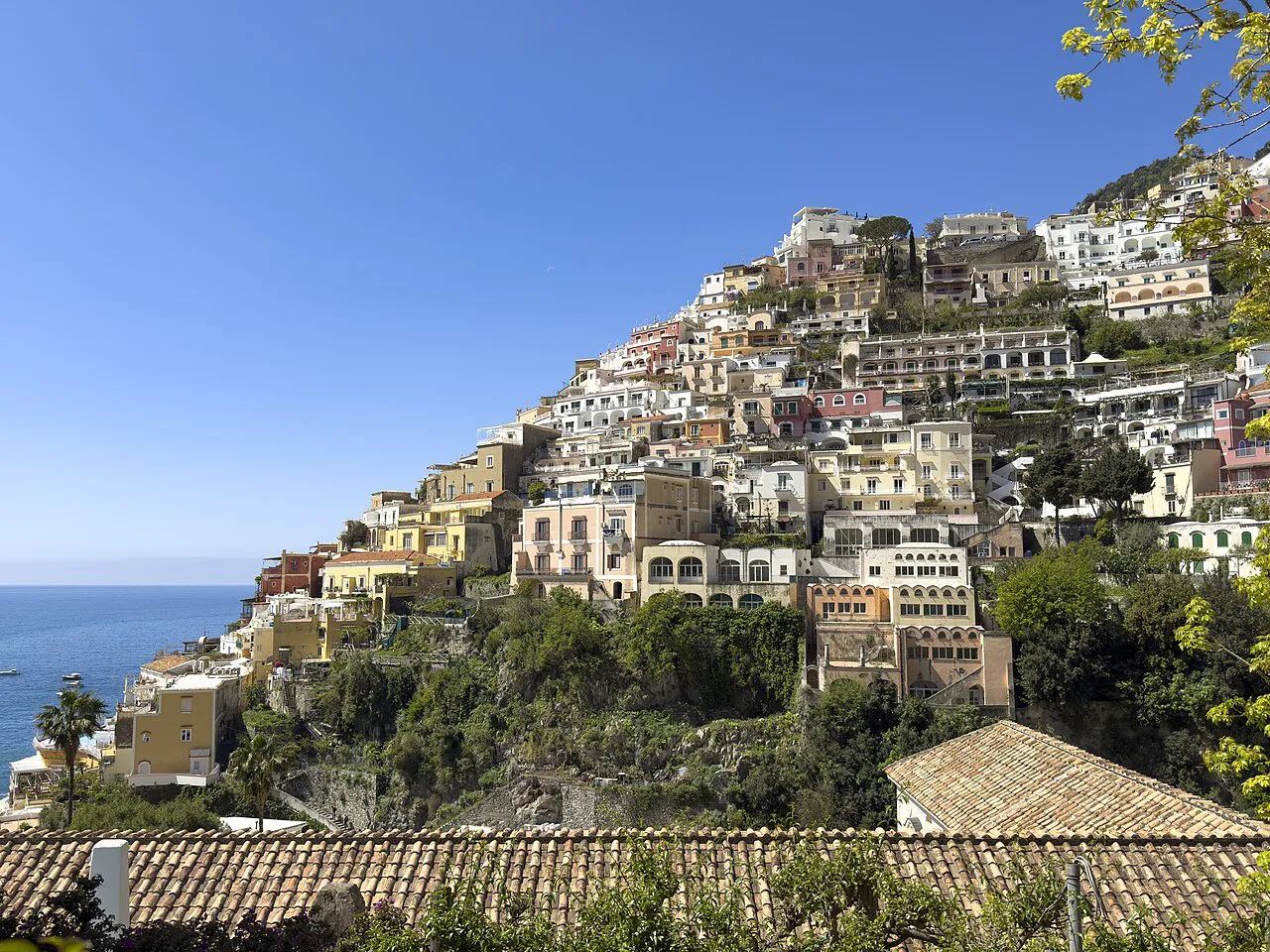 Positano's cream and pastel houses climbing the hillside above the sea, seen over tiled rooftops