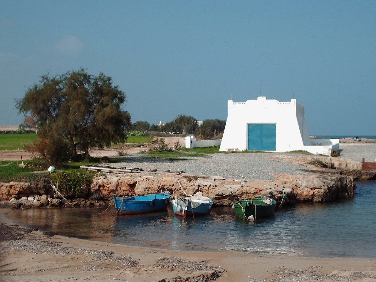 Small fishing boats in a rocky inlet beside a white coastal building at Savelletri di Fasano