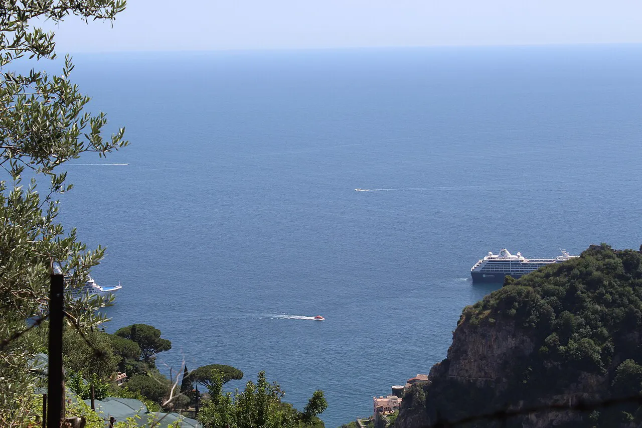 Olive branches framing the open Gulf of Salerno and wooded cliffs below Ravello, a cruise ship offshore