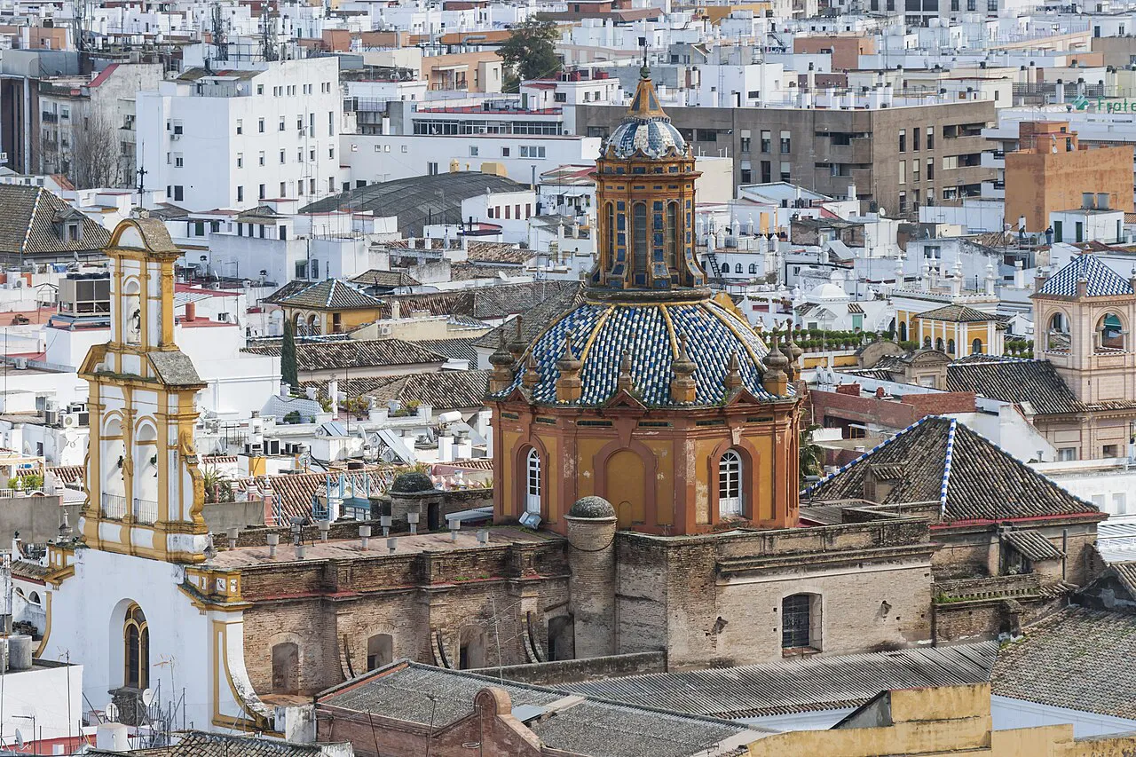 Tiled church dome and bell tower rising above the rooftops of Seville, seen from the Giralda