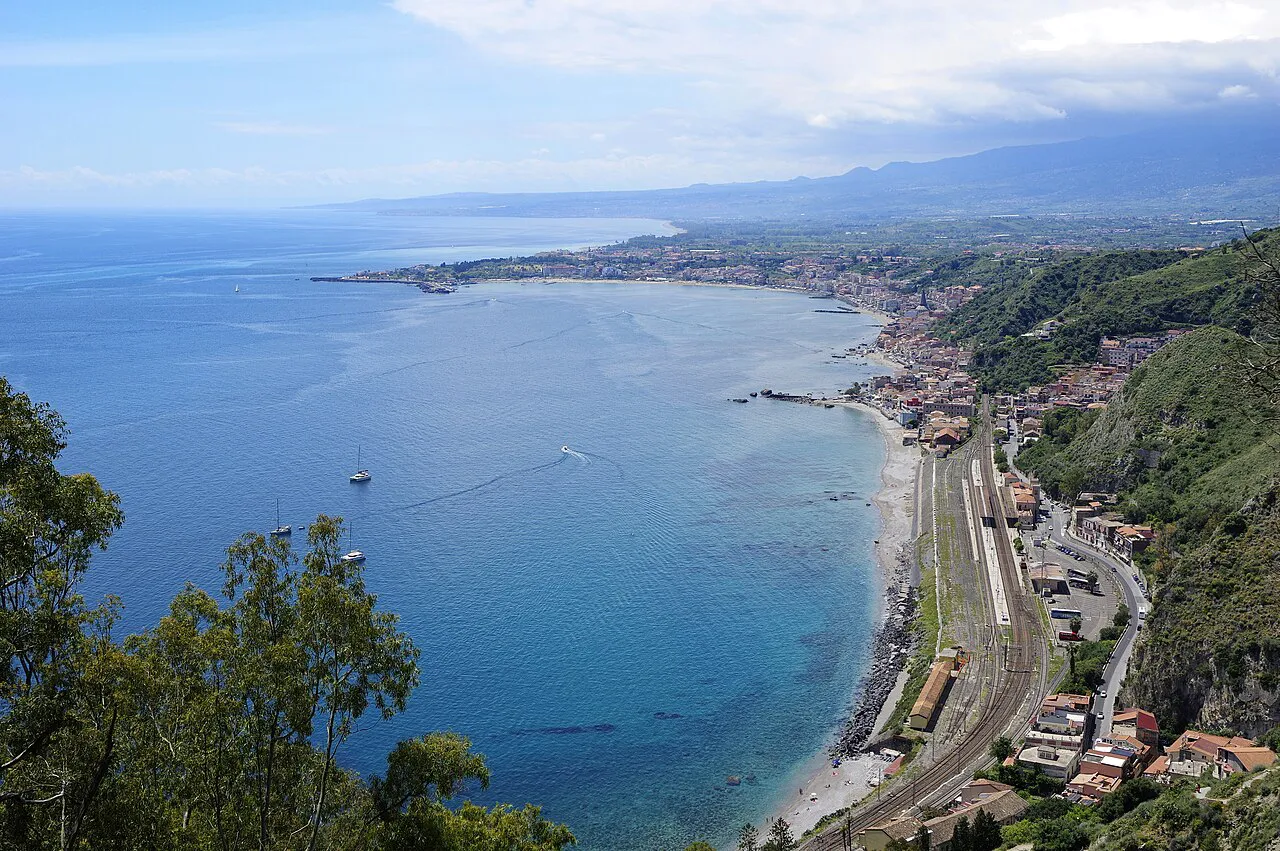 The coastline below Taormina curving towards Giardini Naxos, with the railway along the shore and Etna’s slopes