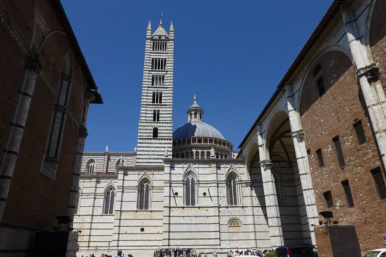The striped marble bell tower and dome of Siena Cathedral seen between tall brick walls