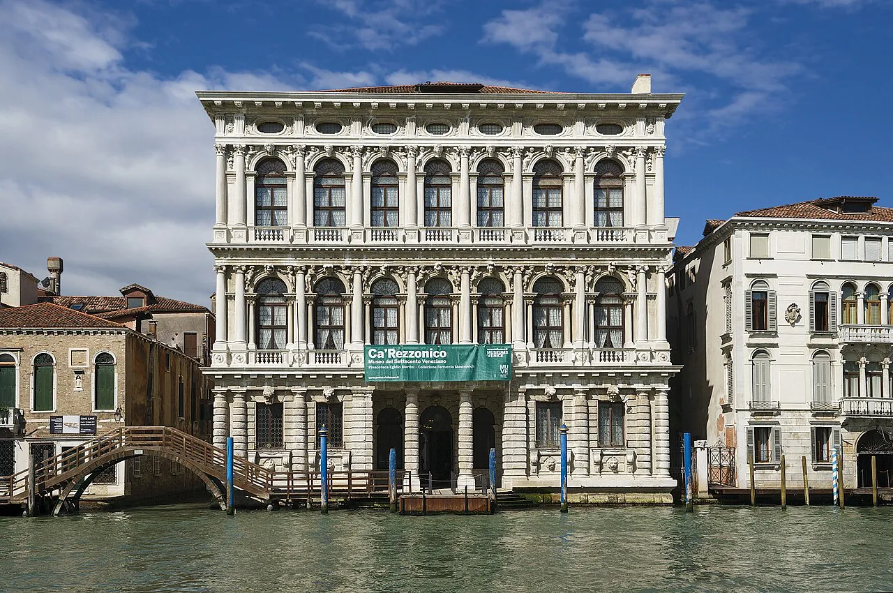 Baroque facade of Ca’ Rezzonico on the Grand Canal in Venice under a blue sky