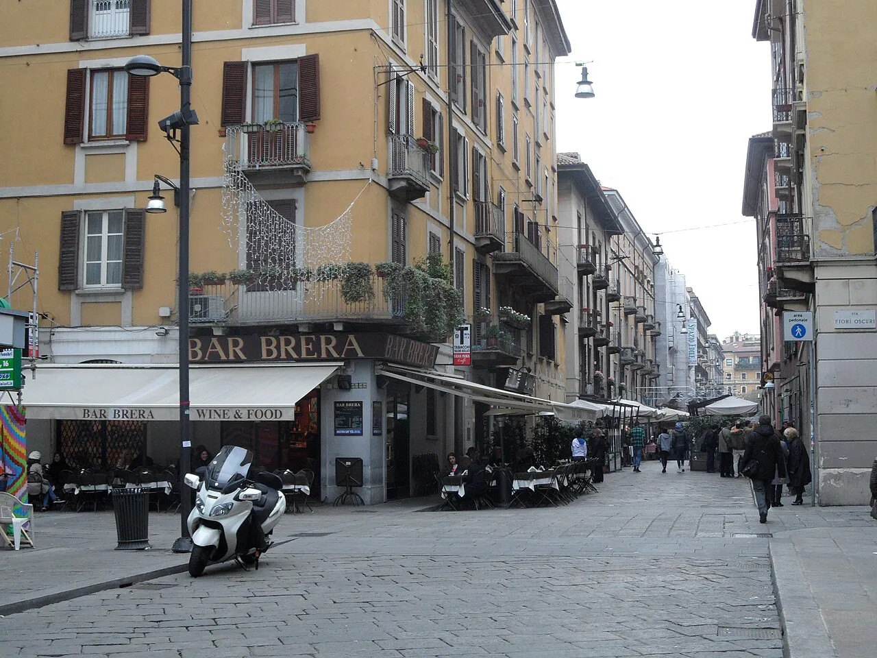 Cobbled Brera street corner in Milan with ochre apartment buildings and pavement café tables
