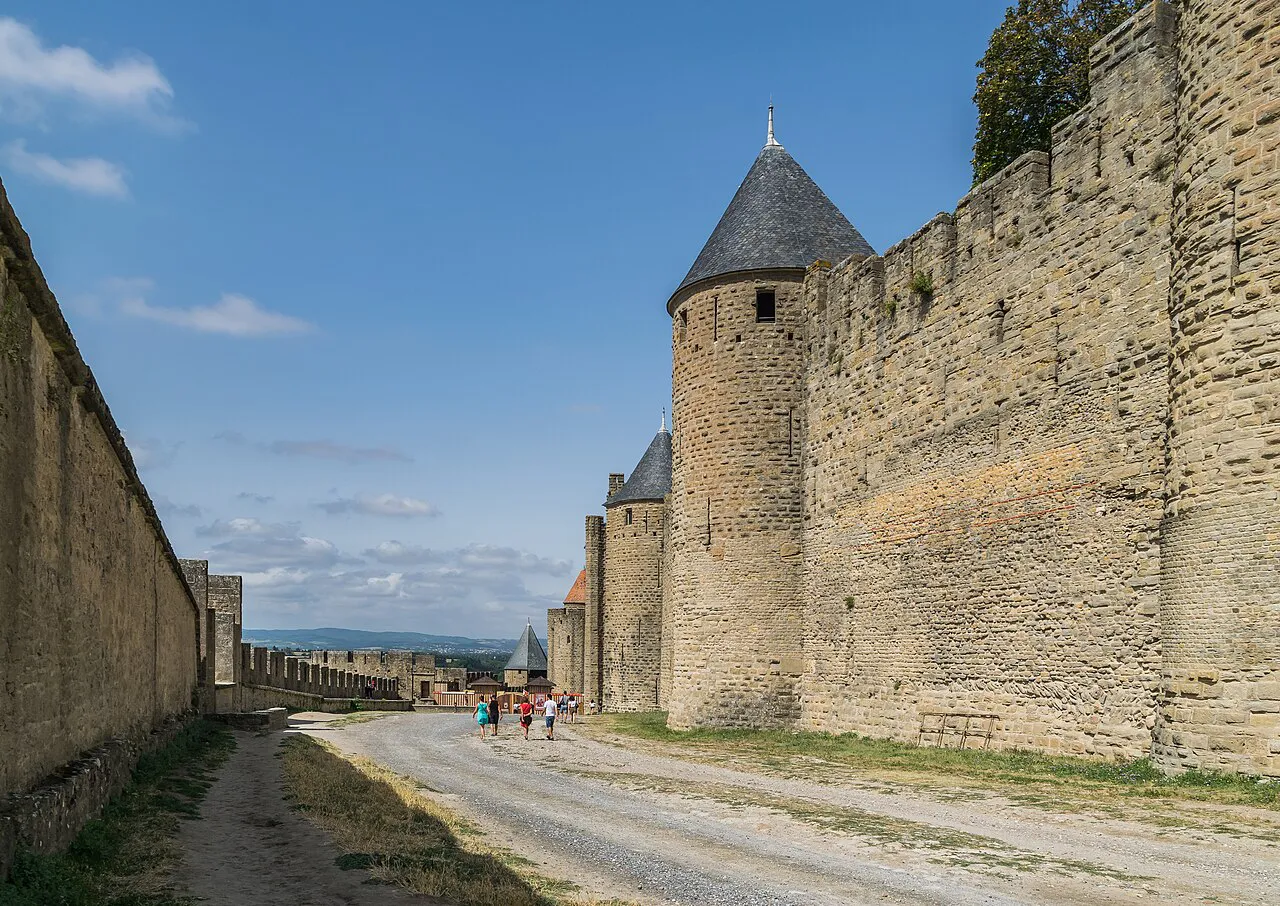 Path between the ramparts and pointed-roof towers of the Cité de Carcassonne under a blue sky