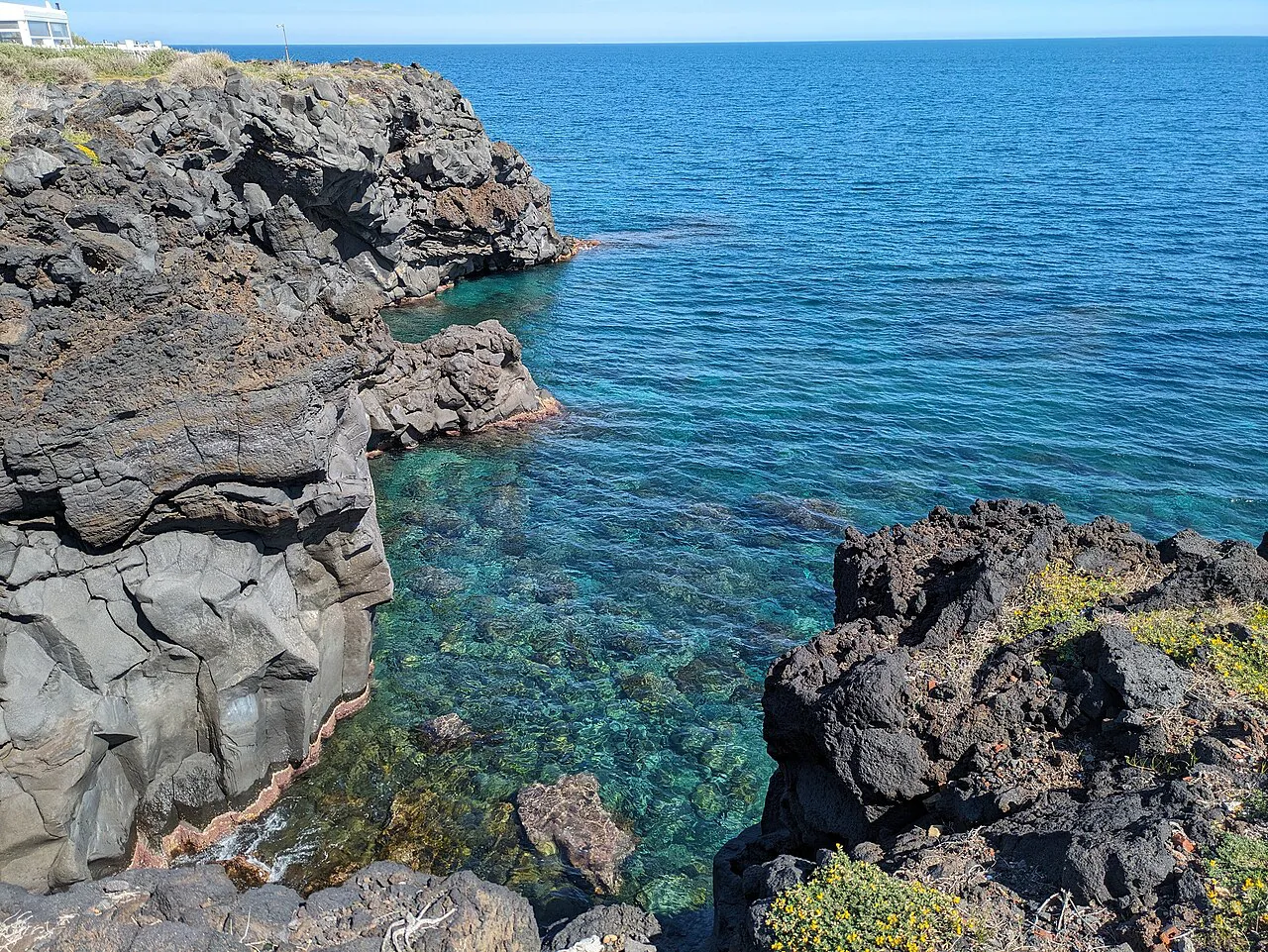 Black lava rocks framing clear turquoise sea water along the Catania lungomare