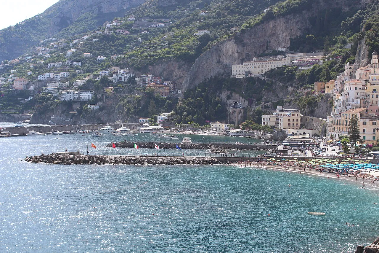 Amalfi's beach and harbour breakwater below the town and wooded cliffs of the Amalfi Coast