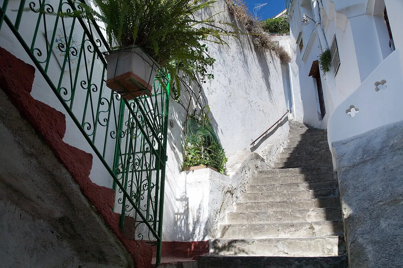 Narrow whitewashed stepped lane with an iron railing and potted plants in Amalfi