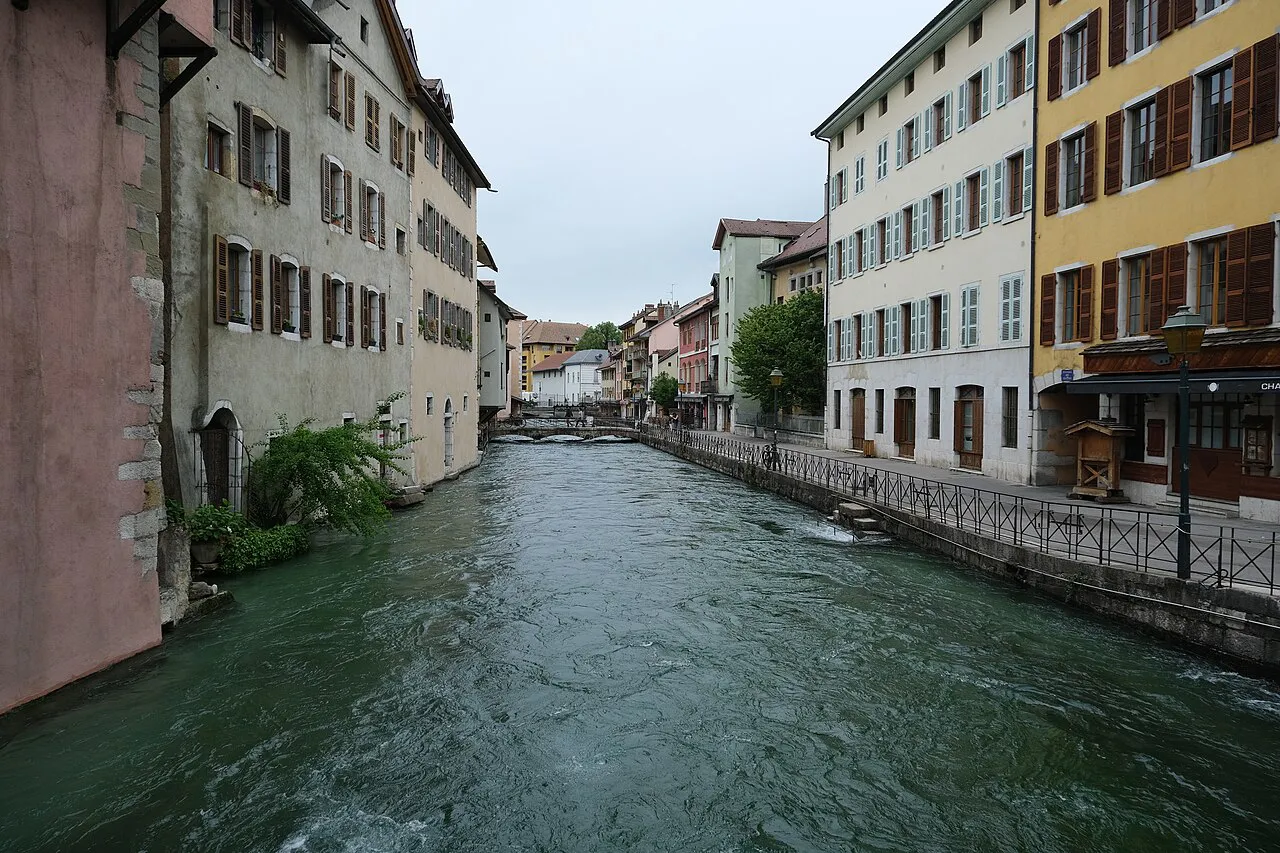 Wide view of the Thiou river flowing between pastel buildings and railings in Annecy old town