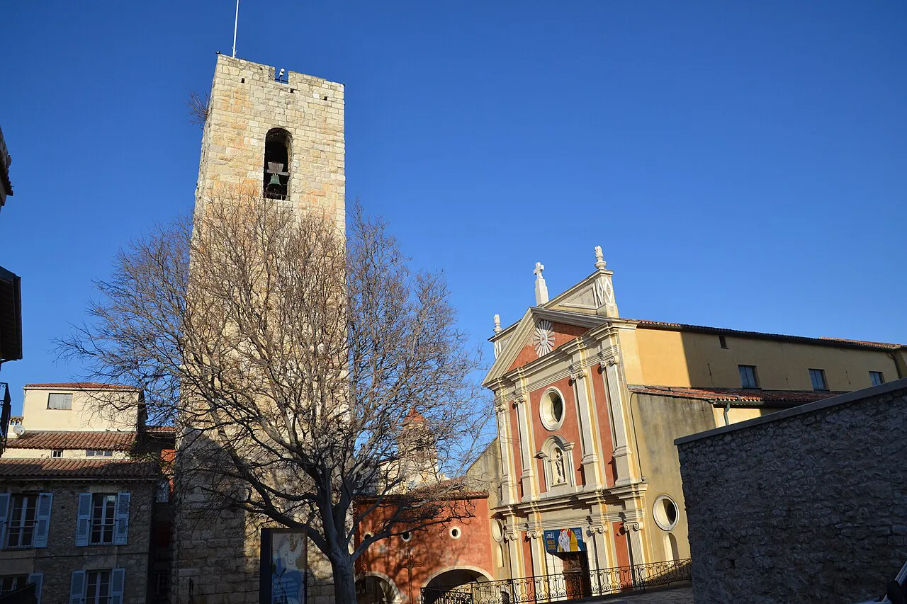 Stone Saracen tower beside the ochre facade of Antibes cathedral under a clear blue sky