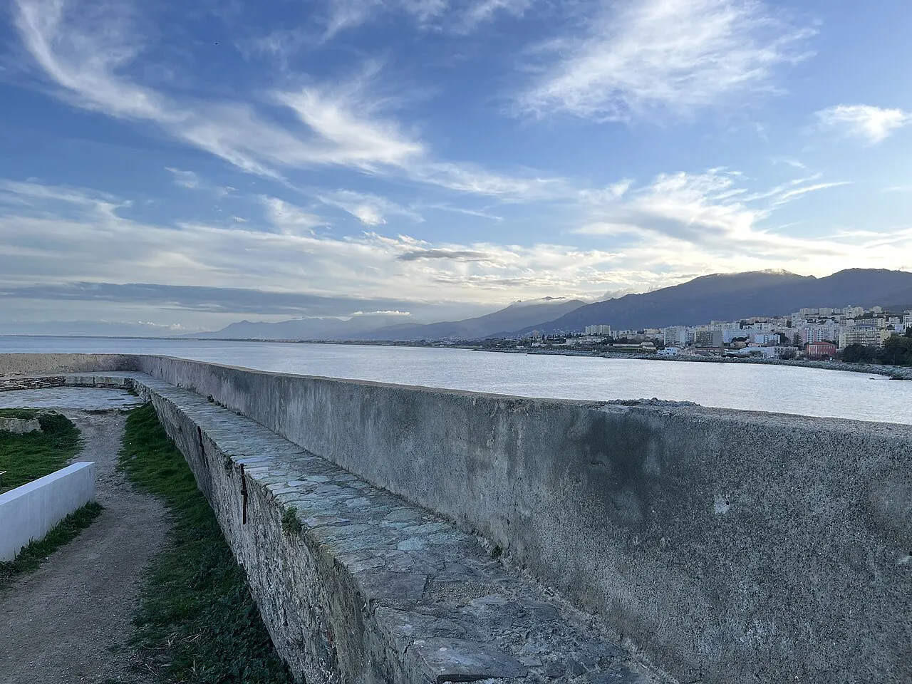 Rampart walkway of the Bastia citadel above the sea, with the coastline and hills beyond