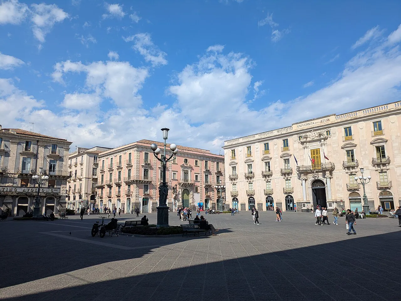 Wide paved Piazza Università in Catania with a central lamp post and baroque palazzi under a blue sky