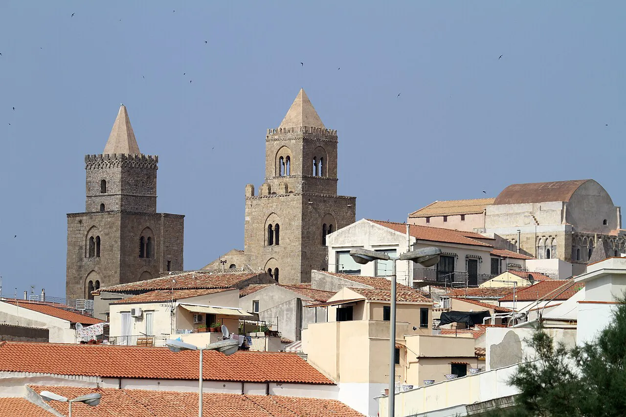 The twin towers of Cefalù Cathedral rising above terracotta rooftops, seen from the seafront