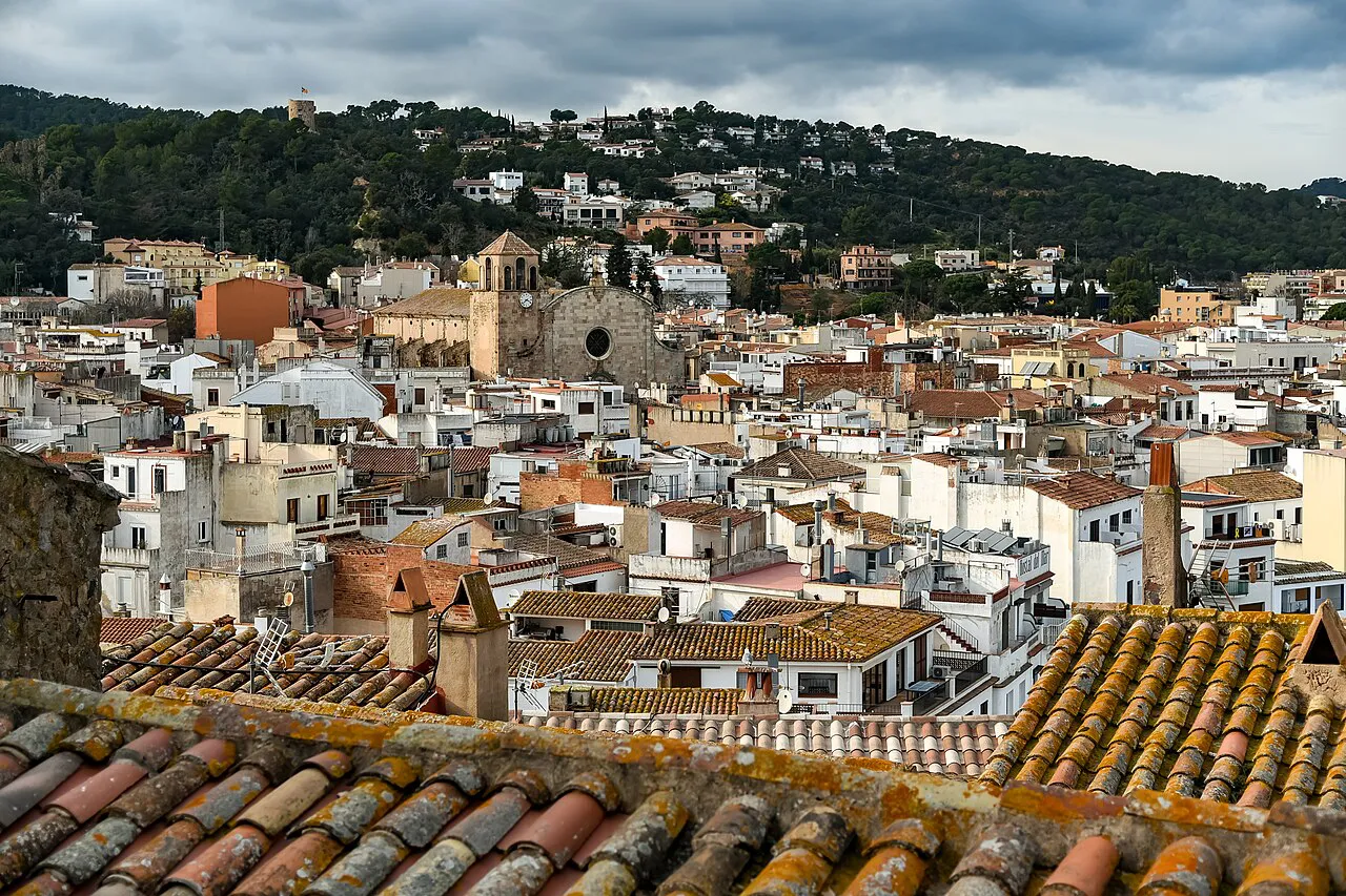 Tiled rooftops of Tossa de Mar's town centre and parish church below wooded hills